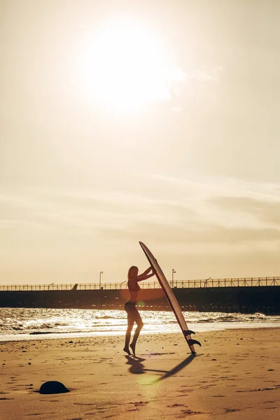 Surferin posiert mit Surfbrett am Strand bei Sonnenuntergang — Stockfoto