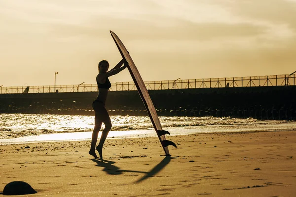 Silhouette einer Surferin posiert mit Surfbrett am Strand bei Sonnenuntergang — Stockfoto