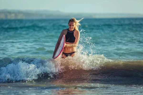 Rubia surfista femenina con tabla de surf en el agua - foto de stock