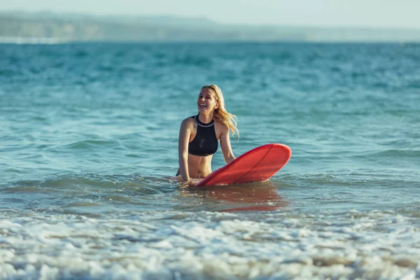 Beautiful female surfer sitting on surfboard in sea — Stock Photo