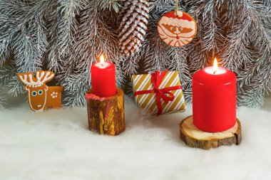 Ahşap standları üzerinde köknar dalları ile hafif karlı bir arka plan üzerinde Noel zencefilli kurabiye, hediyeler ve mumlar vardır.
