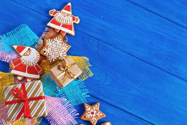 Christmas gingerbread cookies, gifts on the background of colored coarse cloth, wooden blue