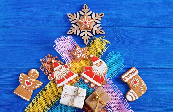 Christmas gingerbread cookies, gifts on the background of colored coarse cloth, wooden blue