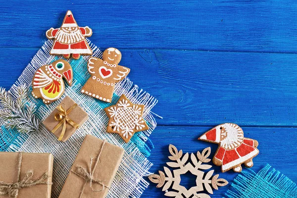 Christmas gingerbread cookies, gifts and fir branches on a blue wooden background and pieces of colored fabric