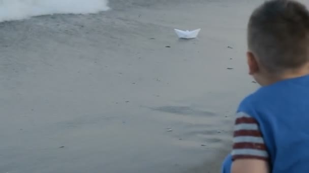 Хлопчик запускає паперовий корабель у морі — стокове відео