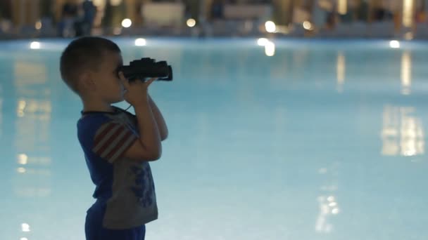 Little boy looks through binoculars near pool — Stock Video