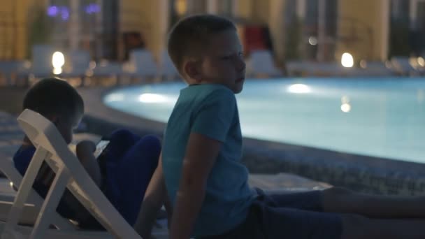 Мальчик играет в игру на смартфоне возле бассейна — стоковое видео