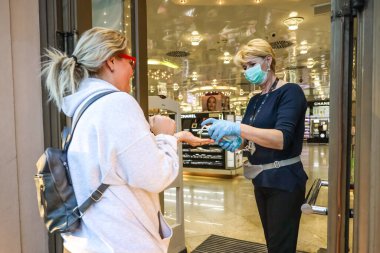 Zagreb, Croatia - March 19, 2020 : A shop employee stands at the entrance and disinfects the hands of shoppers entering the Muller shop on the Ban Jelacic square because of corona virus crisis. clipart