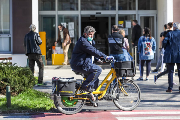 Velika Gorica, Croatia - March 19, 2020 : People on the street of Velika Gorica wear protective masks because of corona virus crisis. Postman on the electric bike wear protective masks.