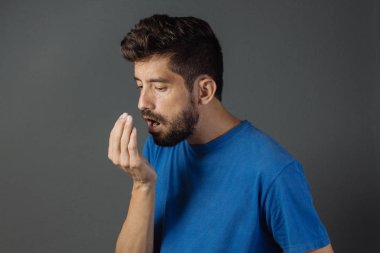 Nefesi kokuyor. Ağız kokusu konsepti. Genç adam elleriyle nefesini kontrol ediyor..