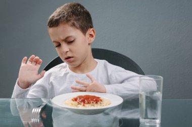 Portrait of child with no appetite in front of the meal. Concept clipart
