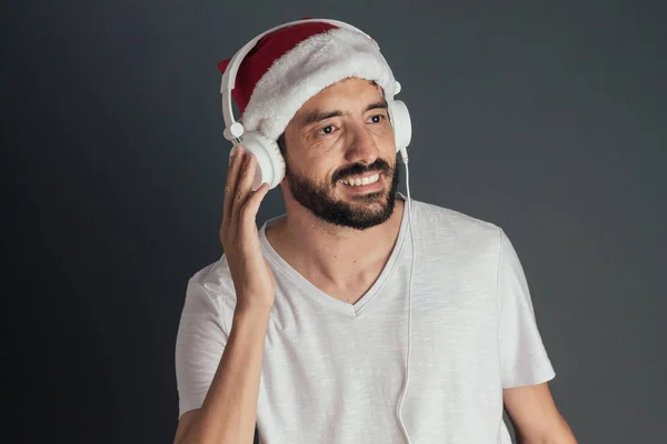Ung man klädd i Santa hatt och T-shirt som lyssnar på musik i hörlurar. — Stockfoto