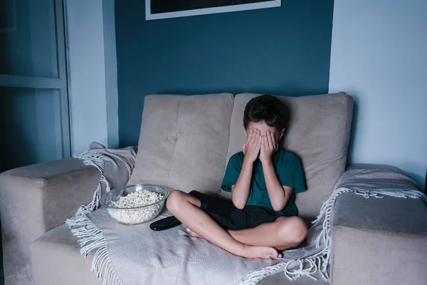 Niño asustado viendo películas de miedo en la televisión, sentado en el sofá por la noche — Foto de Stock