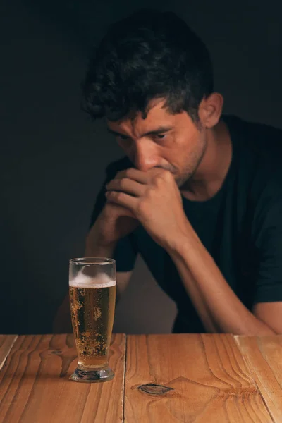 アルコール依存症の概念。暗い部屋でビールのガラスのテーブルに悲しい男. — ストック写真