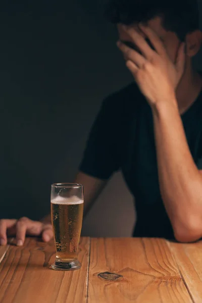 Concept of alcoholism. Sad man at the table with a glass of beer in a dark room. — Stock Photo, Image