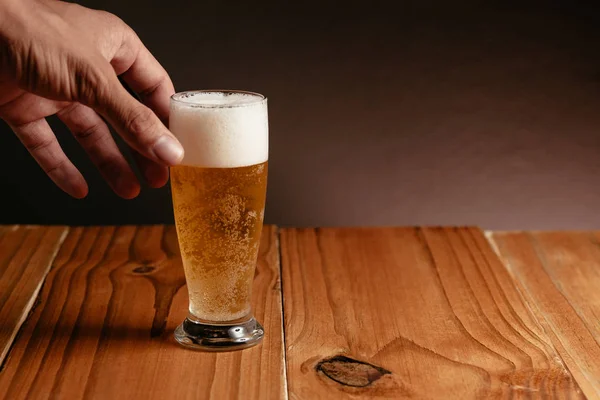Zamknij się w męskiej dłoni przy kuflu piwa z drewna tabela — Zdjęcie stockowe