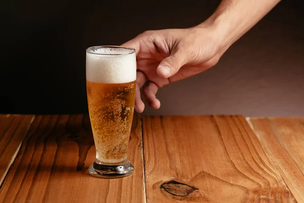 Zamknij się w męskiej dłoni przy kuflu piwa z drewna tabela — Zdjęcie stockowe