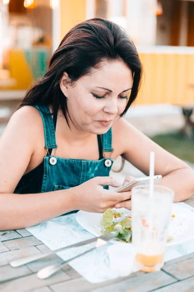 Mujer en restaurante al aire libre disfrutando de su comida y usando smartphone —  Fotos de Stock
