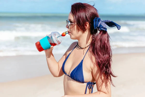 Молодая рыжая женщина пьет клубничный коктейль на пляже — стоковое фото