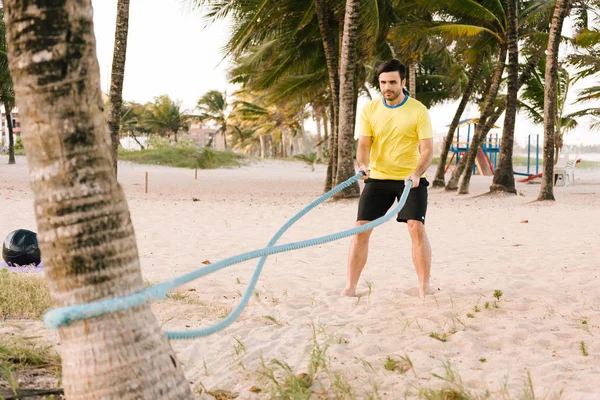 Sportlicher junger Mann trainiert mit Seil am Strand — Stockfoto