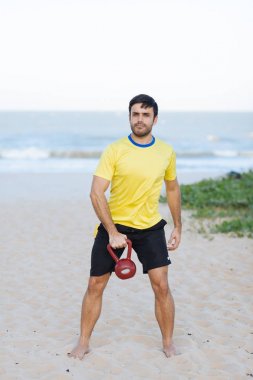 Brezilyalı adam bir ağır kettlebell kumsalda egzersiz sırasında kaldırma