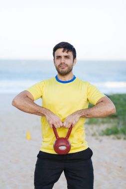 Brezilyalı adam bir ağır kettlebell kumsalda egzersiz sırasında kaldırma