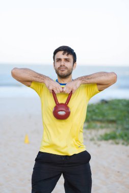 Brezilyalı adam bir ağır kettlebell kumsalda egzersiz sırasında kaldırma