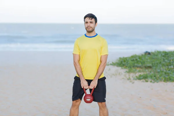 Brezilyalı adam bir ağır kettlebell kumsalda egzersiz sırasında kaldırma — Stok fotoğraf