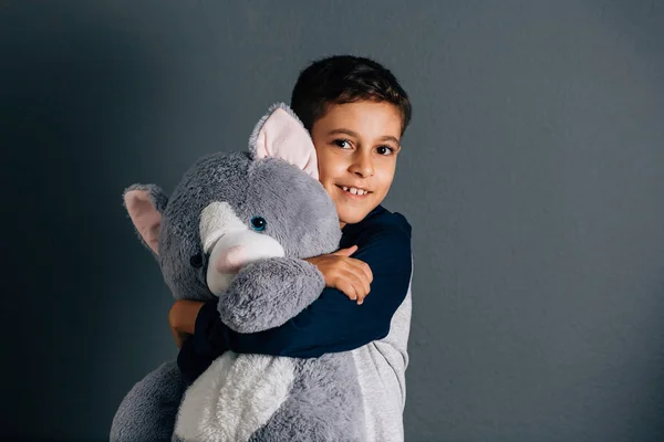 Adorable boy hugging his teddy bear on gray background — Stock Photo, Image