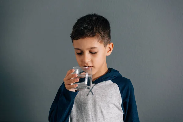 Brazilian little boy drinking water from glass on gray backgroun — Stock Photo, Image