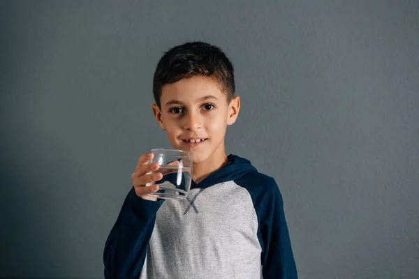 Brazilian little boy drinking water from glass on gray backgroun — Stock Photo, Image