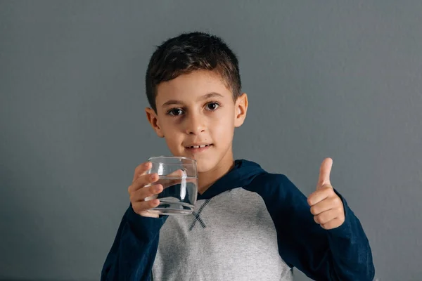 Portrait of boy drinking glass of water and gesturing thumb up — Stock Photo, Image