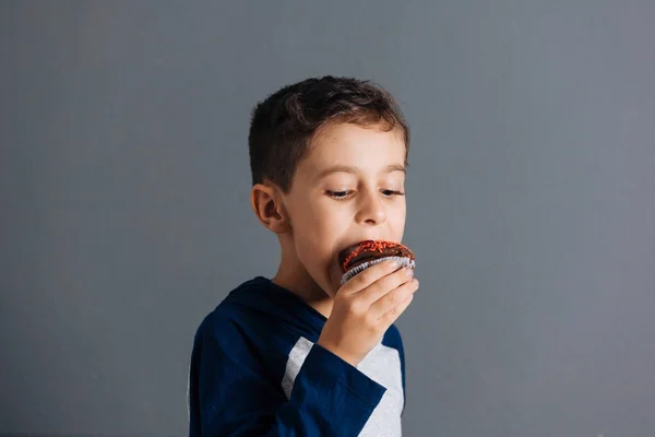 Brazilian child eating cupcake on gray background — Stock Photo, Image