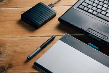 Dizüstü bilgisayar, dış sabit disk ve ahşap arka plan üzerinde grafik tablet.