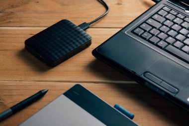 Dizüstü bilgisayar, dış sabit disk ve ahşap arka plan üzerinde grafik tablet.