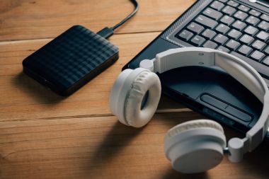 Dizüstü bilgisayar, dış sabit disk ve ahşap arka plan üzerinde kulaklık