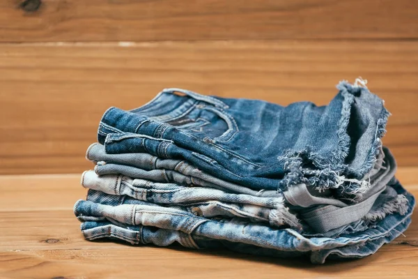 Fashionabla kläder. hög med jeans på en trä bakgrund — Stockfoto