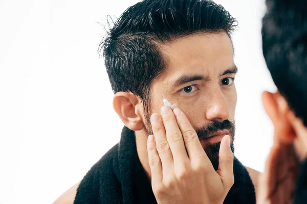 Hombre guapo aplicando crema facial en el baño mientras mira el espejo — Foto de Stock