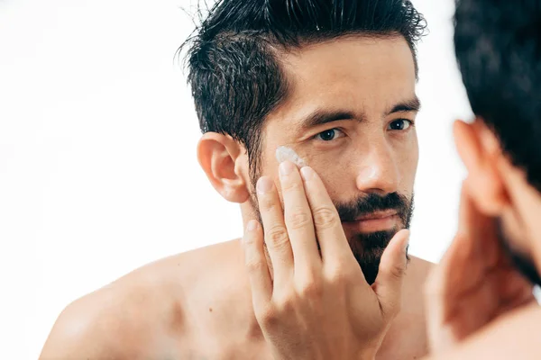 Hombre guapo aplicando crema facial en el baño mientras mira el espejo — Foto de Stock