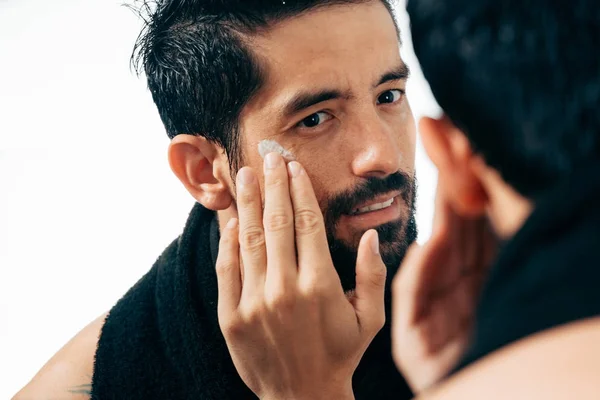 Hombre guapo aplicando crema facial en el baño mientras mira el espejo — Foto de Stock