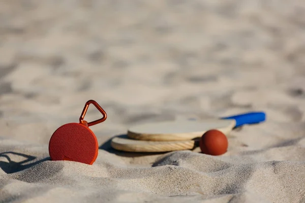 Vezeték nélküli hordozható hangszóró és a strand tenisz ütő a strandon — Stock Fotó