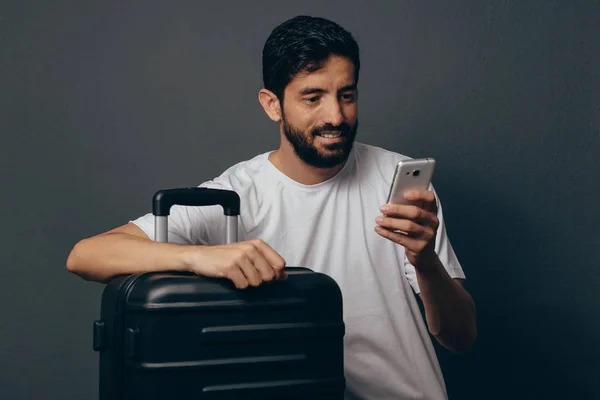 Портрет молодого человека с чемоданом, держащего смартфон — стоковое фото
