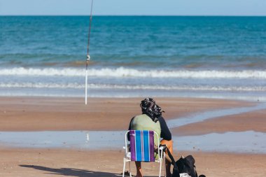 Bazı balık yakalamak için balıkçı sahilde kanca için bekleyen oturuyor