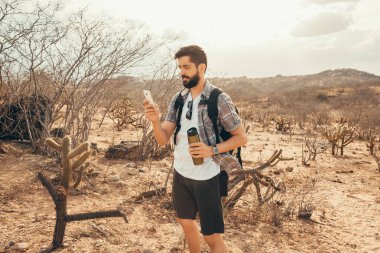 Genç adam gezisinde. Gezgin el akıllı telefon ile dağın günbatımında dinleniyor.