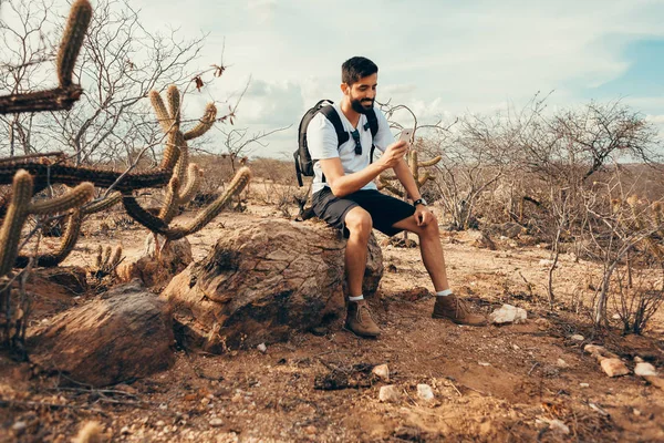 Jonge man op de reis. Reiziger met slimme telefoon in de hand rust op de top van berg bij de zonsondergang. — Stockfoto