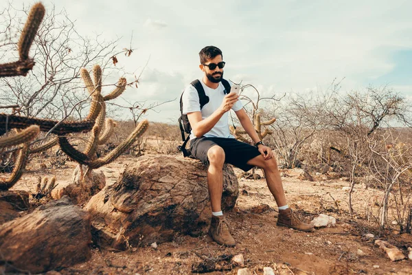 Молодой человек в поездке. Путешественник со смартфоном в руке отдыхает на вершине горы на закате . — стоковое фото