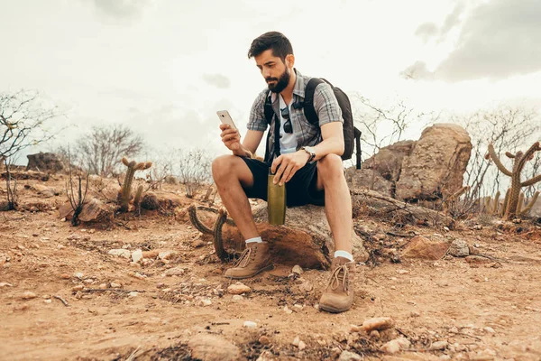 Anak muda dalam perjalanan. Pelancong dengan ponsel pintar di tangan sedang beristirahat di puncak gunung saat matahari terbenam . — Stok Foto