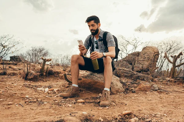 Ung man på resan. Resenär med smart telefon i handen vilar på toppen av berget vid solnedgången. — Stockfoto