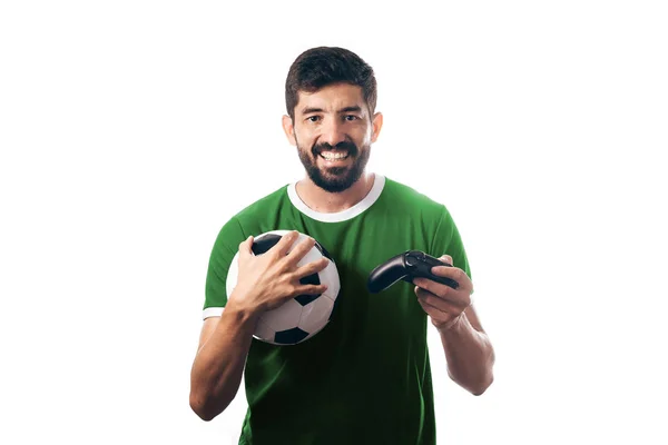 Ποδόσφαιρο ή το ποδόσφαιρο ανεμιστήρα φορώντας πράσινη στολή και κρατώντας μια μπάλα και ένα joystick σε λευκό φόντο — Φωτογραφία Αρχείου