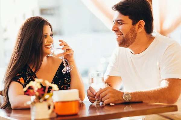 Pasangan muda yang jatuh cinta duduk di sebuah kafe, minum air, bercakap-cakap dan menikmati waktu yang dihabiskan satu sama lain . — Stok Foto